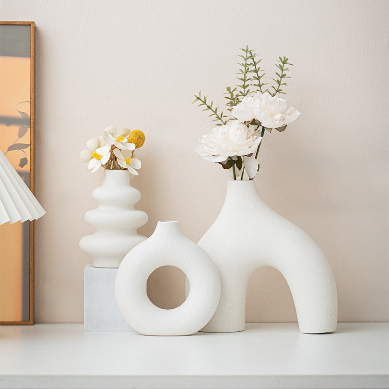 Tre vita keramikvaser med blommor på en hylla