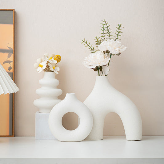 Tre vita keramikvaser med blommor på en hylla