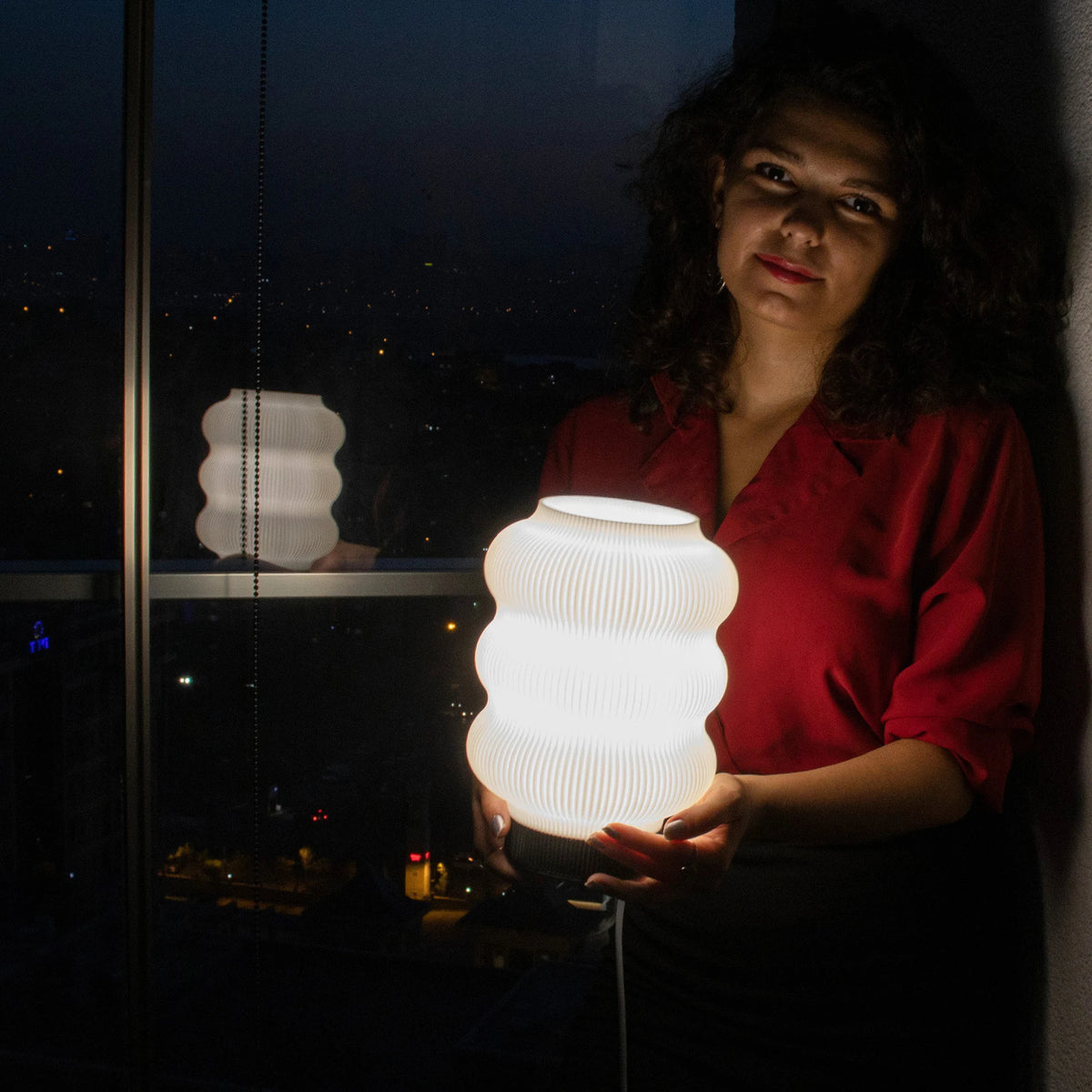 Vågformad 3D-printad bordslampa på sidobord med bok och växt